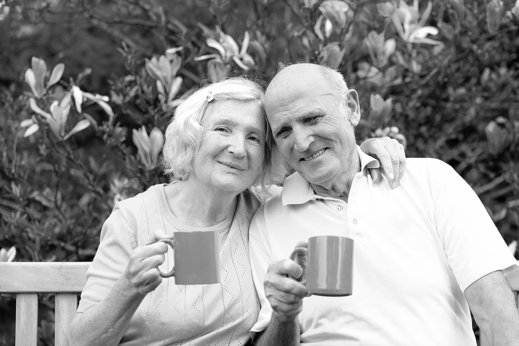 An older couple smiling together over cups of tea