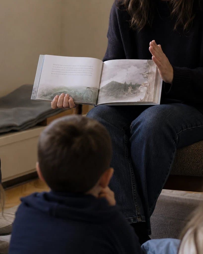 An adult reading a picture book aloud to a small group of children
